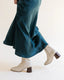 Person wearing a teal satin skirt and white ankle boots on a light background