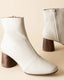 Pair of white ankle boots with wooden block heels on a beige background